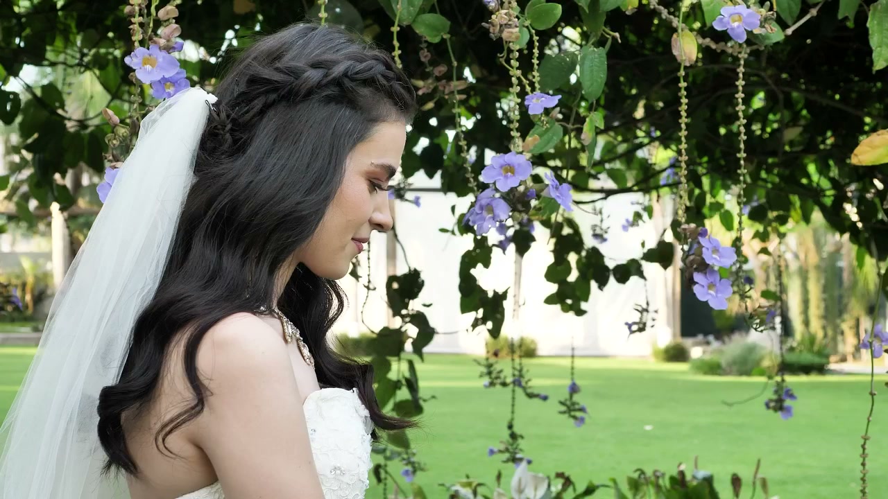 Sous une arche fleurie, une mariée sourit tandis que son mari la rejoint.